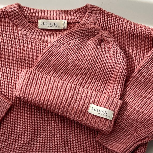 Pink knitted sweater and beanie set on a light background