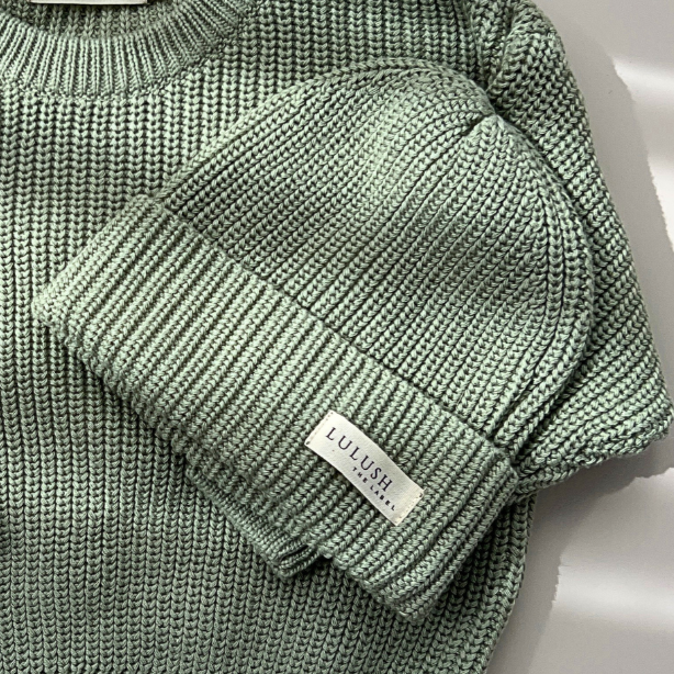 Green knitted sweater and matching beanie on a light background