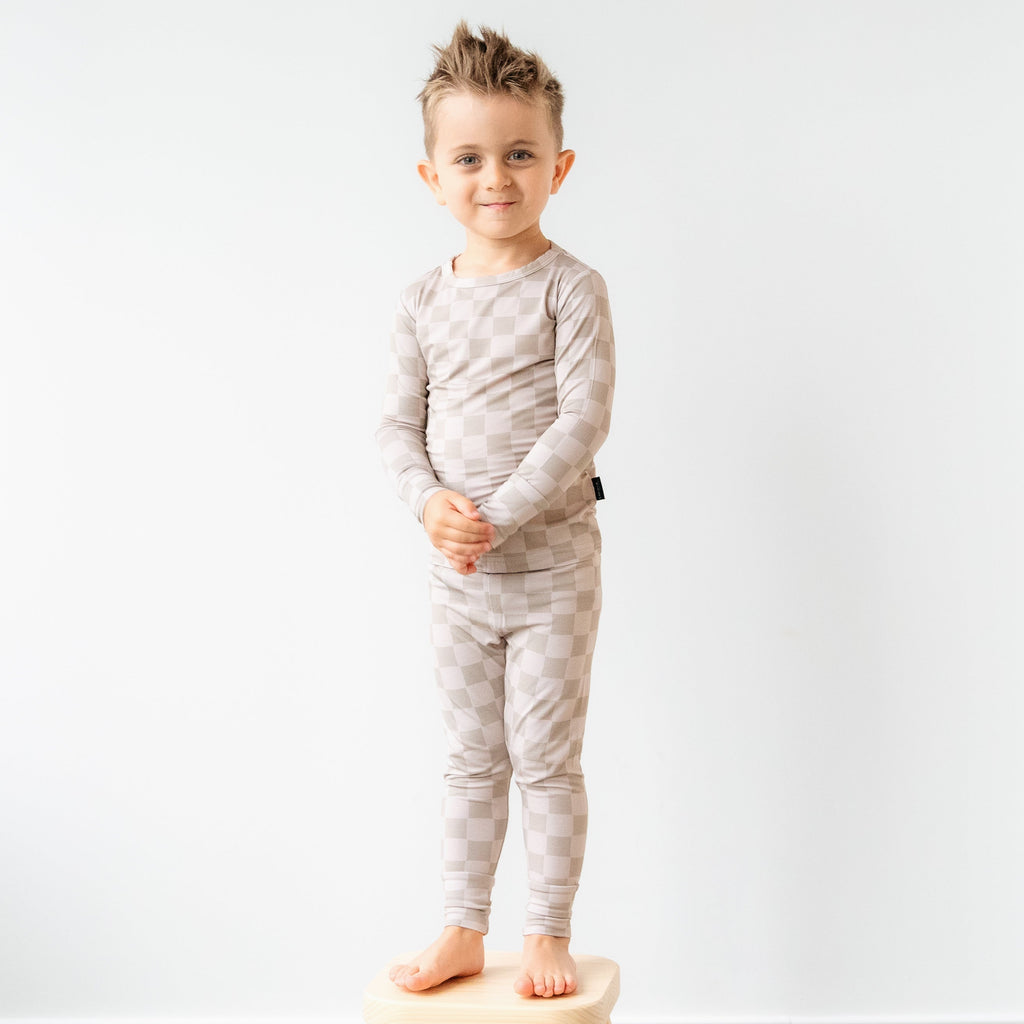 Child wearing a gray pajama set standing on a stool against a white wall
