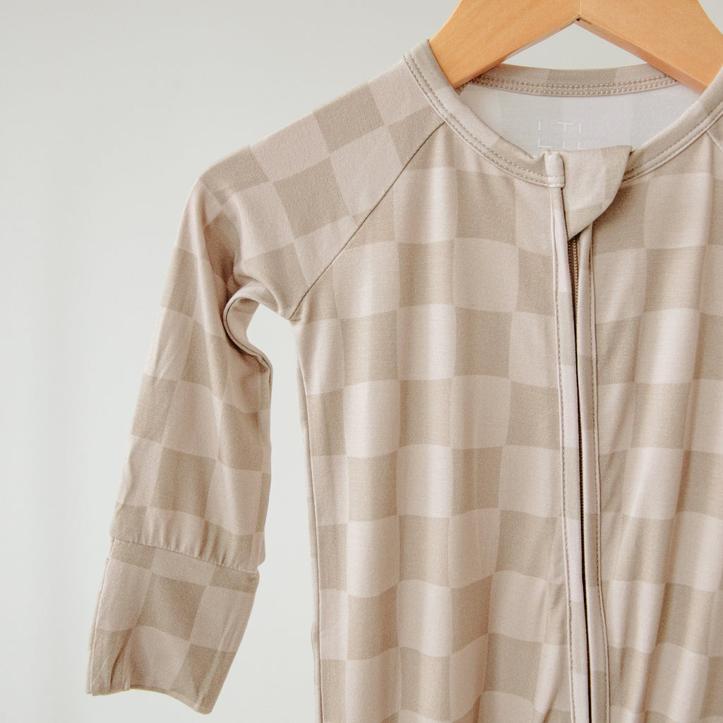Beige checkered baby onesie on a wooden hanger against a white background