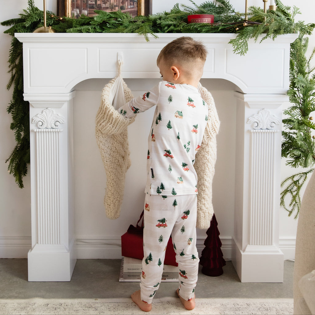 Child in pajamas standing in front of a decorated fireplace with Christmas decorations.