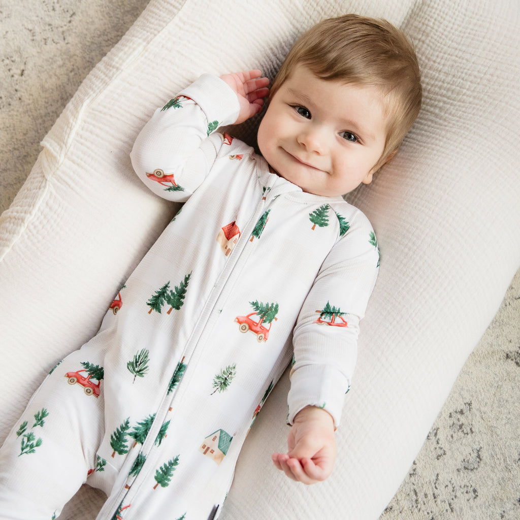 Baby lying on a soft surface wearing a white onesie with nature-themed print