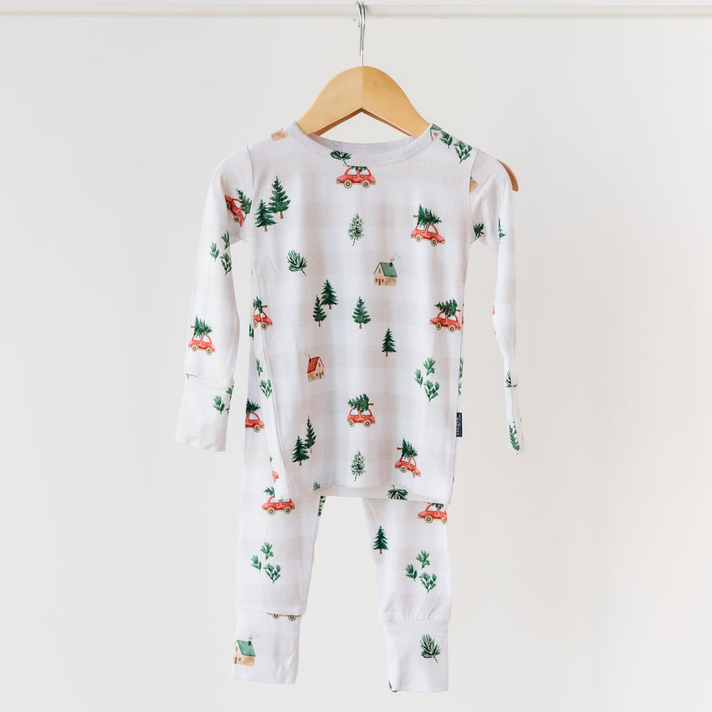 White onesie with car and tree pattern on a wooden hanger against a white background