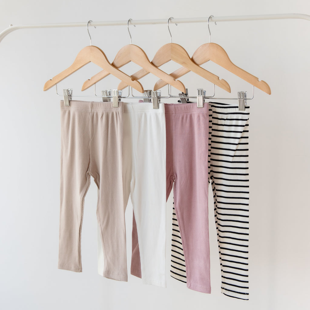 Four pairs of leggings in beige, pink, and black and white stripes hanging on wooden hangers against a white background.