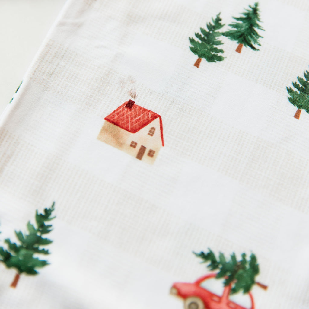Close-up of fabric with Christmas-themed pattern including houses, trees, and cars.
